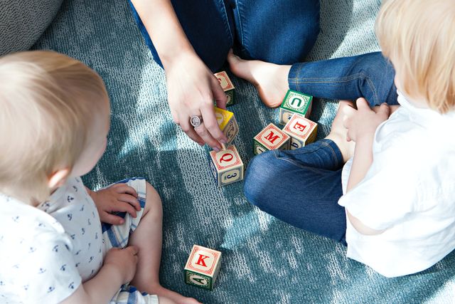 Kleine Kinder und eine erwachsene Person spielen mit Bauklötzen, auf denen Buchstaben und Zahlen stehen